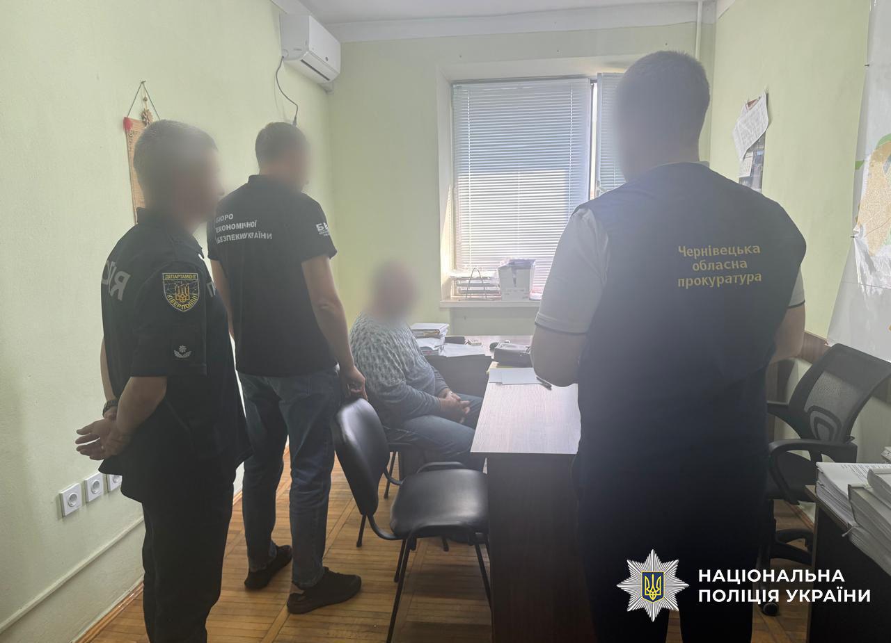 У кабінеті сидить чоловік, поруч стоять кіберполіцейський, детектив БЕБ та представник прокуратури. На столі лежать папери, у кімнаті видно вікно з жалюзі та карту на стіні.
