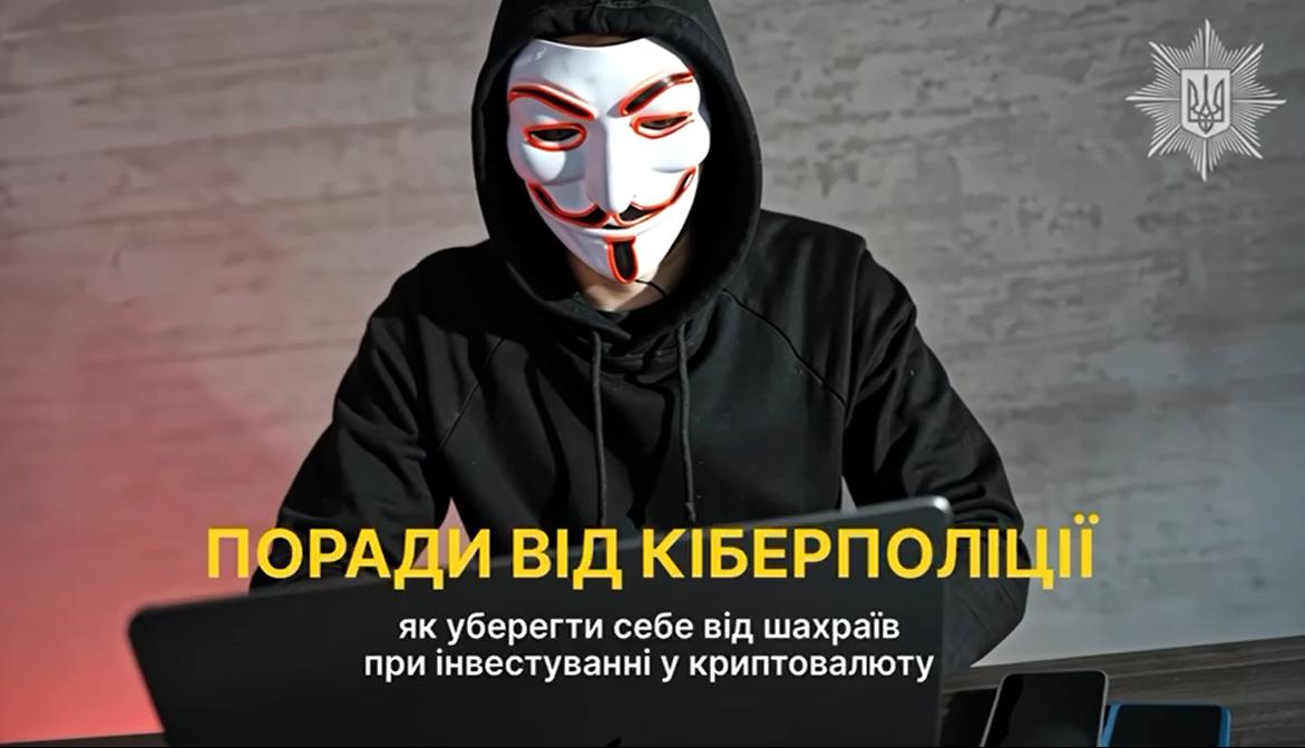 На зображенні чоловік у чорному худі з капюшоном та в масці Гая Фокса сидить за ноутбуком у темному приміщенні. Перед ним на столі лежать кілька смартфонів. У верхньому правому куті розміщено емблему Кіберполіції України. По центру напис жовтими та білими літерами: Поради від кіберполіції: як уберегти себе від шахраїв при інвестуванні у криптовалюту.