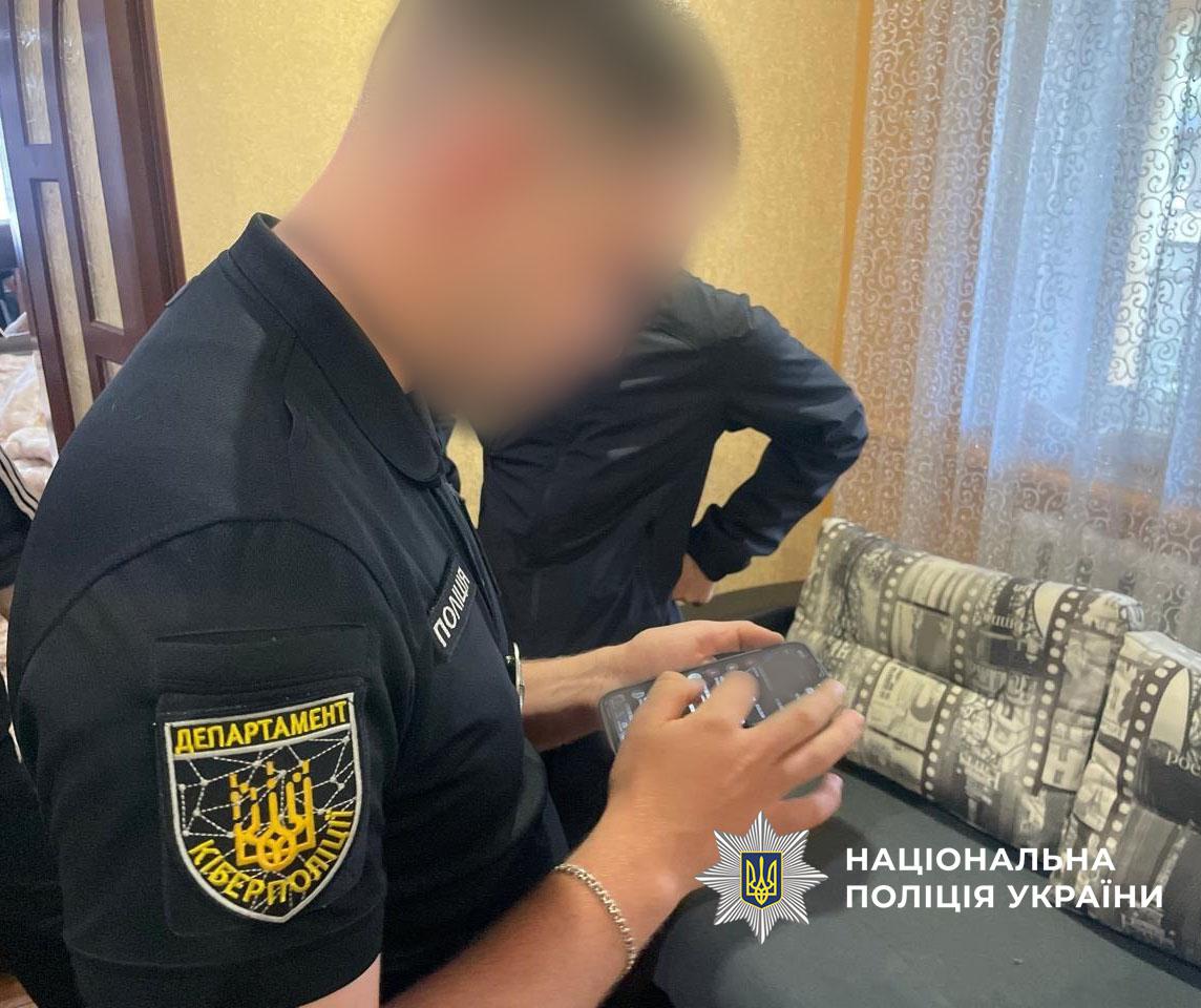 На фотографії в інтер'єрі кімнати зображено двох людей крупним планом збоку. На передньому плані ліворуч стоїть чоловік у чорній футболці-поло, на правому рукаві якої розміщена нашивка у формі щита із гербом України, павутиною та написами ДЕПАРТАМЕНТ і КІБЕРПОЛІЦІЯ, а на грудях видно напис ПОЛІЦІЯ. Чоловік тримає в руках мобільний телефон та натискає пальцем на його екран. Його обличчя повністю розмите. За ним стоїть інший чоловік у темній куртці, повернутий спиною або боком до камери, його обличчя також розмите. Праворуч на задньому плані розташований диван із сіро-білими подушками, прикрашеними принтом у вигляді кіноплівки, та вікно із прозорою візерунчастою шторою. Стіни кімнати мають жовтуватий відтінок. У правому нижньому куті кадру розміщено білу емблему у вигляді восьмикутної зірки з гербом України всередині та напис білими літерами НАЦІОНАЛЬНА ПОЛІЦІЯ УКРАЇНИ.