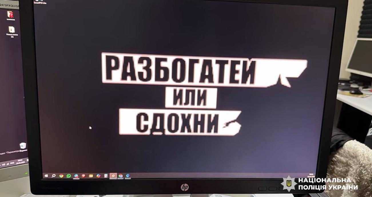 Світлина монітора комп'ютера бренду HP з чорною рамкою, на якому відкрито зображення на темному тлі з великим текстовим написом у три рядки. Російськомовний текст виконано великими чорними літерами всередині трьох білих прямокутних блоків із нерівними краями: у першому рядку написано РАЗБОГАТЕЙ, у другому — ИЛИ, у третьому — СДОХНИ. У нижній частині екрана видно панель завдань операційної системи з іконками програм. Ліворуч частково видно край другого монітора з робочим столом. У правому нижньому кутку поверх фотографії накладено білий логотип-зірку з гербом-тризубом на синьому тлі та білий напис Національна поліція України.