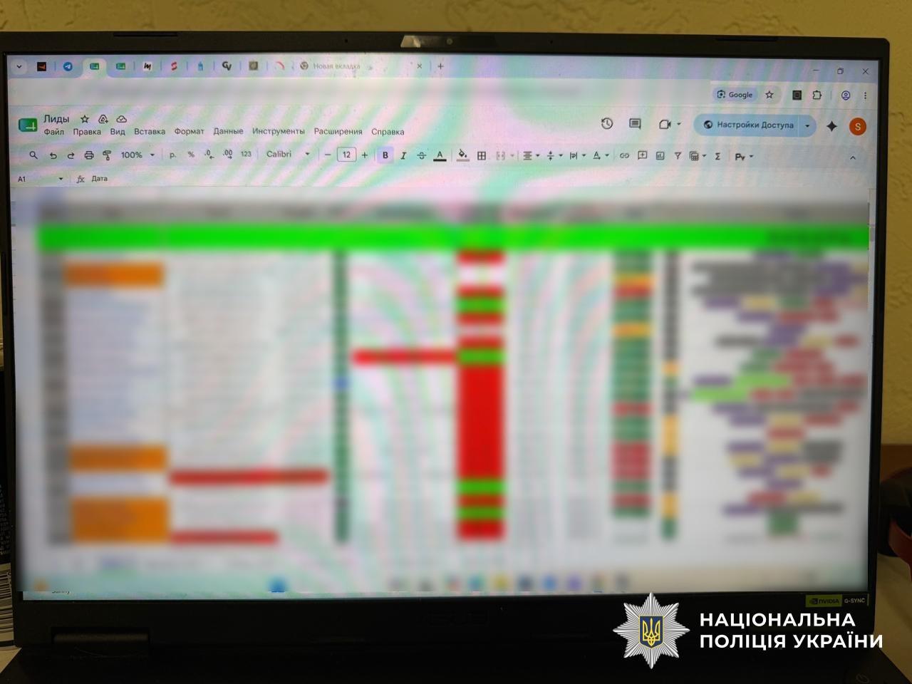 Світлина екрана ноутбука, на якому відкрито електронну таблицю Google Таблиці з назвою Лиды. Вся область таблиці з комірками, текстом та кольоровими позначками повністю сильнo розмита, через що окремі дані та написи неможливо прочитати. У верхній частині екрана видно стандартну панель інструментів веббраузера та меню редагування таблиці. У правому нижньому кутку на чорній рамці ноутбука поверх фотографії накладено білий логотип-зірку з гербом-тризубом на синьому тлі та білий напис Національна поліція України.